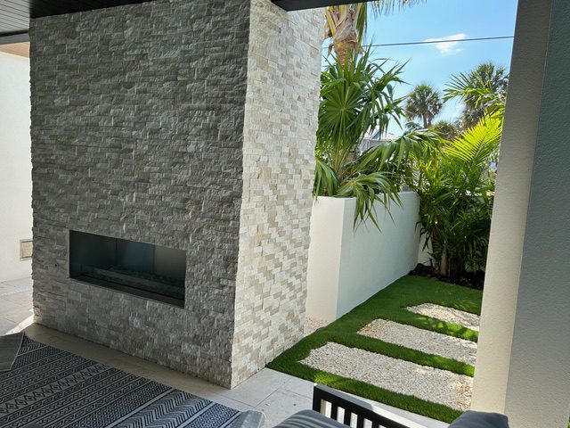 Modern patio with stone fireplace and greenery.