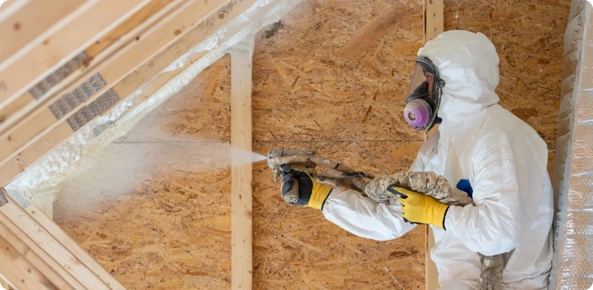Worker spraying insulation in attic space.