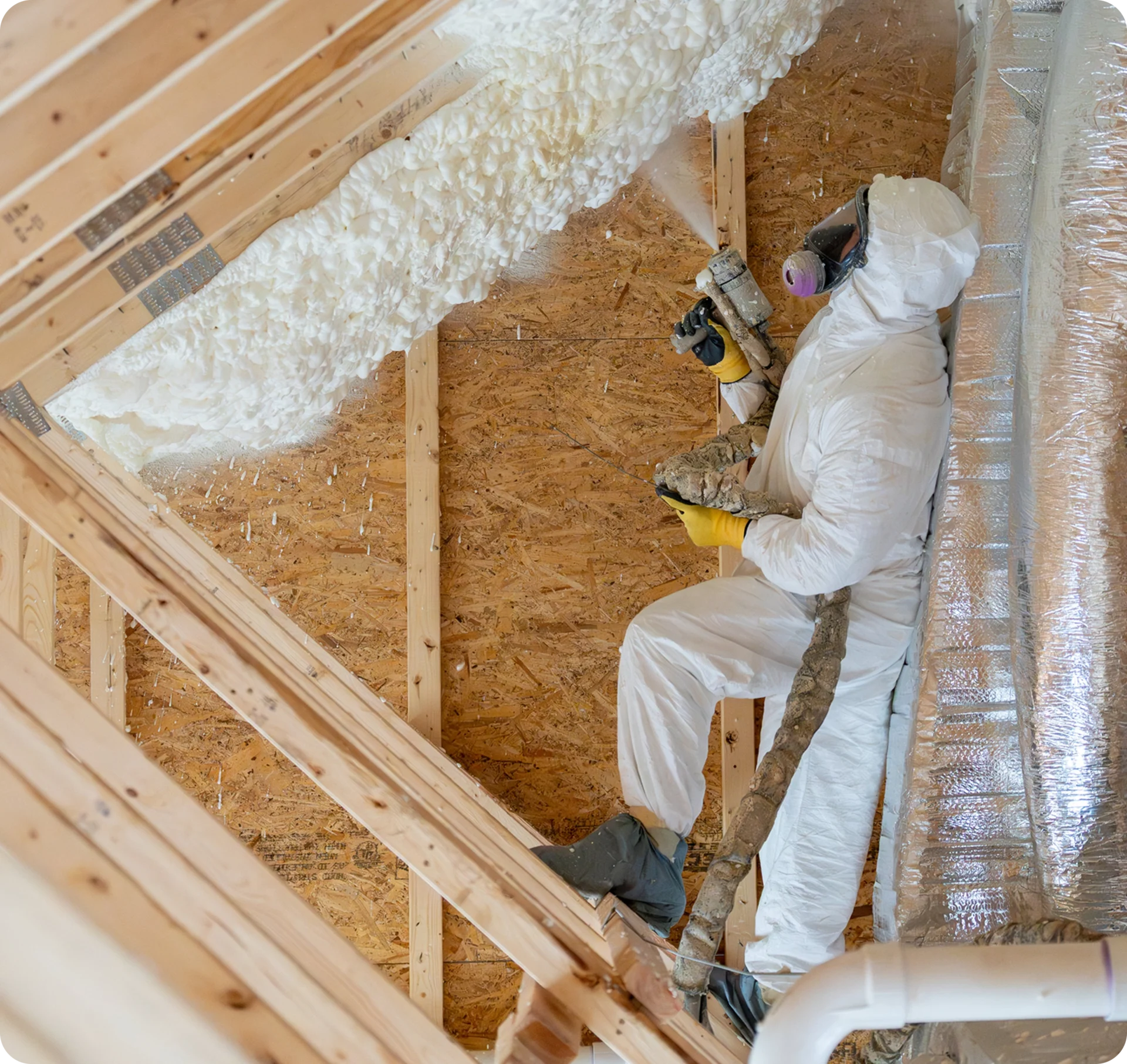 Worker spraying insulation in attic space.