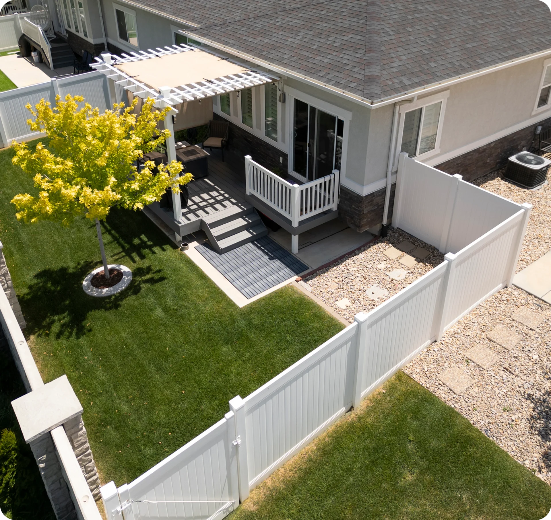 Backyard with tree, patio, and white fence.